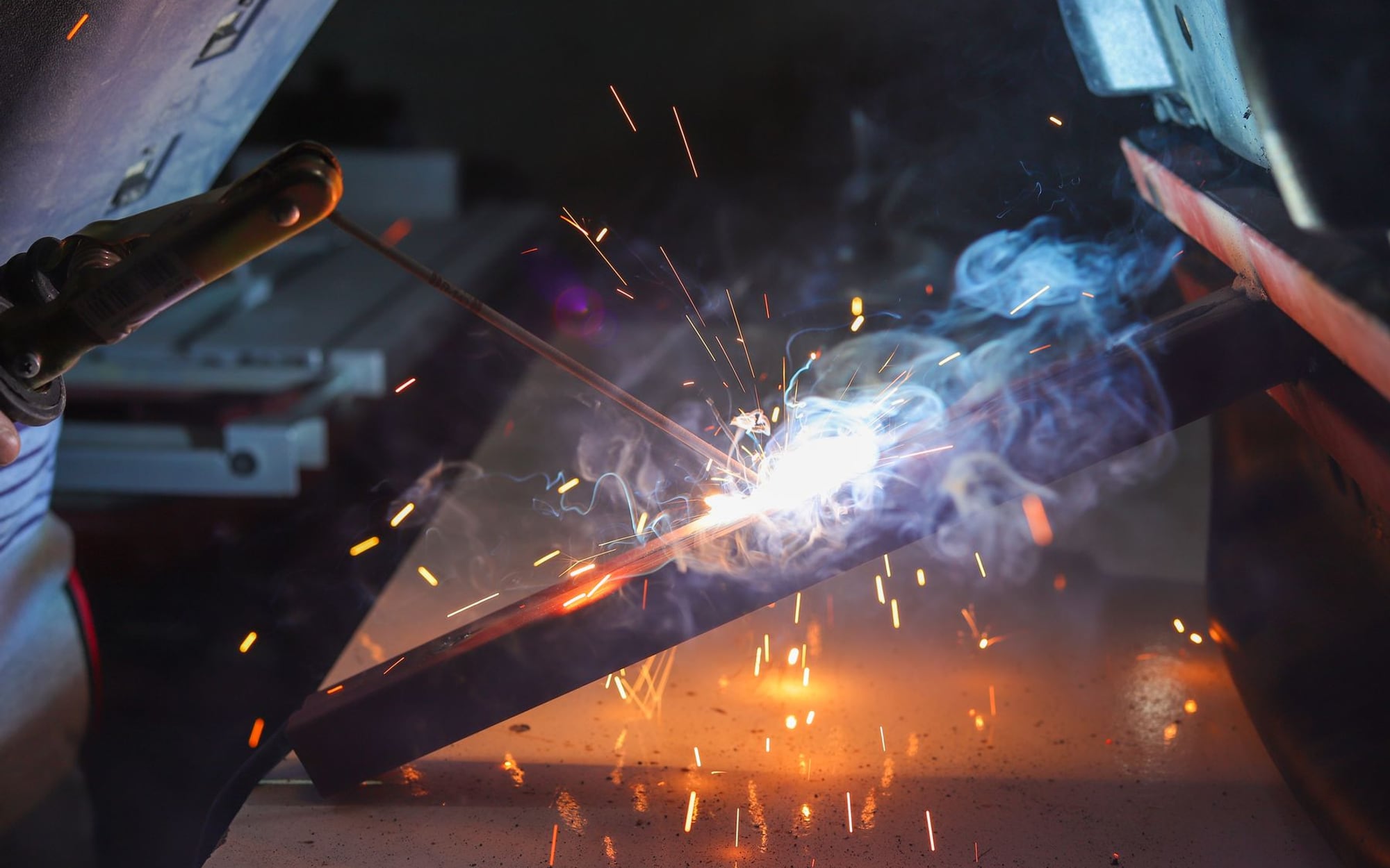 A live welding arc burning along a length of steel angle, sparks and fume rising off the joint &mdash; representative imagery, not a specific Late Night Fabrication job